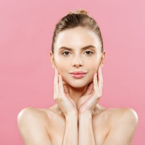 Beauty Spa Concept - Caucasian Woman with perfect face skin Portrait. Beautiful Brunette Spa Girl showing empty copy space. Isolated on pink studio background. Proposing a product. Gesture for advertisement.